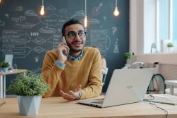 Man talking on phone at desk with laptop.